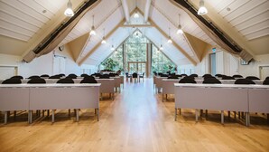 Uma sala de conferências com teto alto, vigas de madeira e uma grande janela no final.