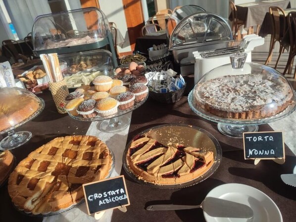 A buffet with various desserts including a lattice-topped pie, a tart, and a cake.
