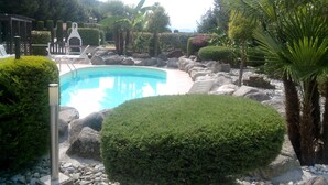A swimming pool surrounded by rocks and various shrubs. - Empire Resort (Iseo)