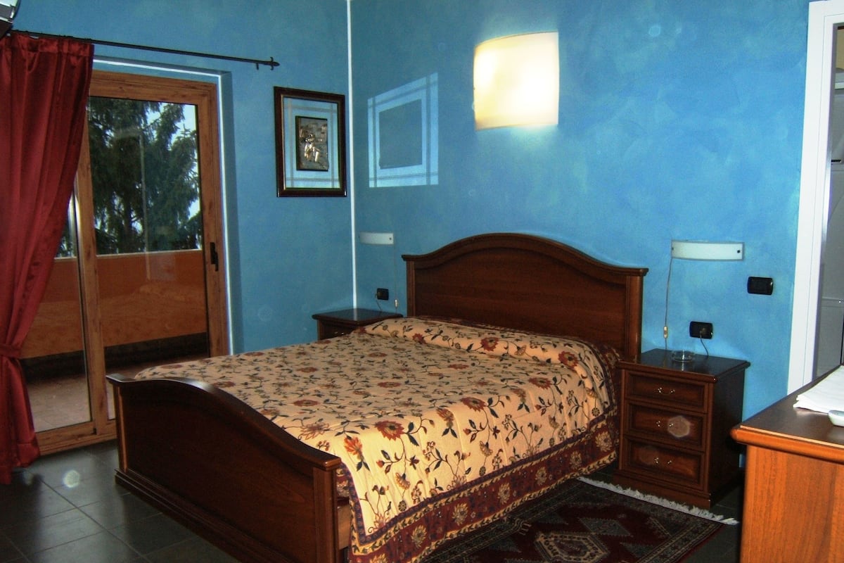 Un dormitorio con cama de madera, mesita de noche, cómoda, alfombra y ventana con cortinas.
