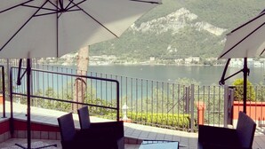 An outdoor patio with tables and chairs, large umbrellas, and a view of a lake and mountains. - Empire Resort (Iseo)