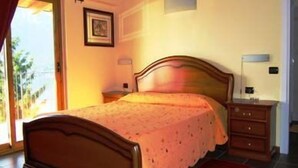 A bedroom with a wooden bed, a nightstand, a lamp, and a window with curtains. - Empire Resort (Iseo)