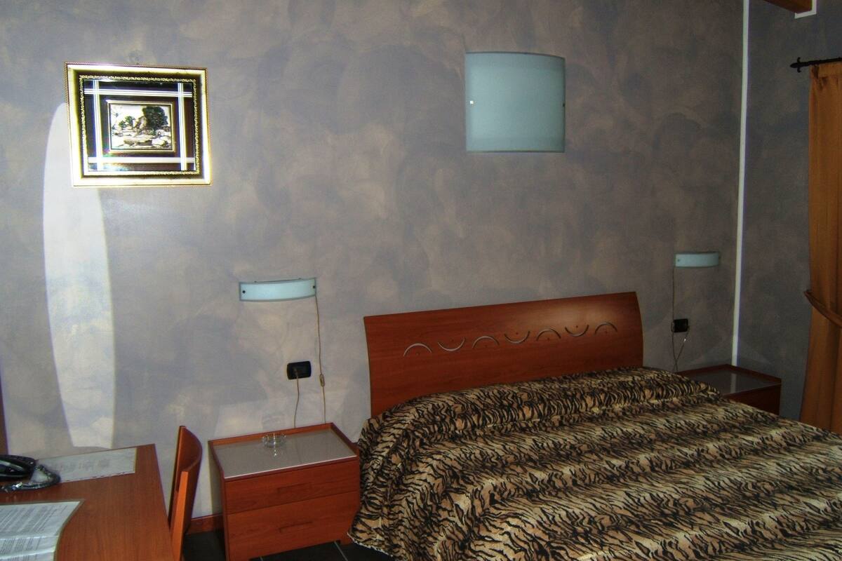 Un dormitorio con una cama de madera, una mesita de noche, un escritorio y un cuadro enmarcado en la pared.