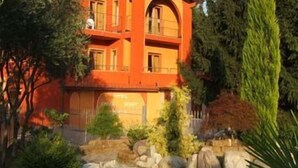A multi-story building with a red facade, surrounded by trees and rocks. - Empire Resort (Iseo)
