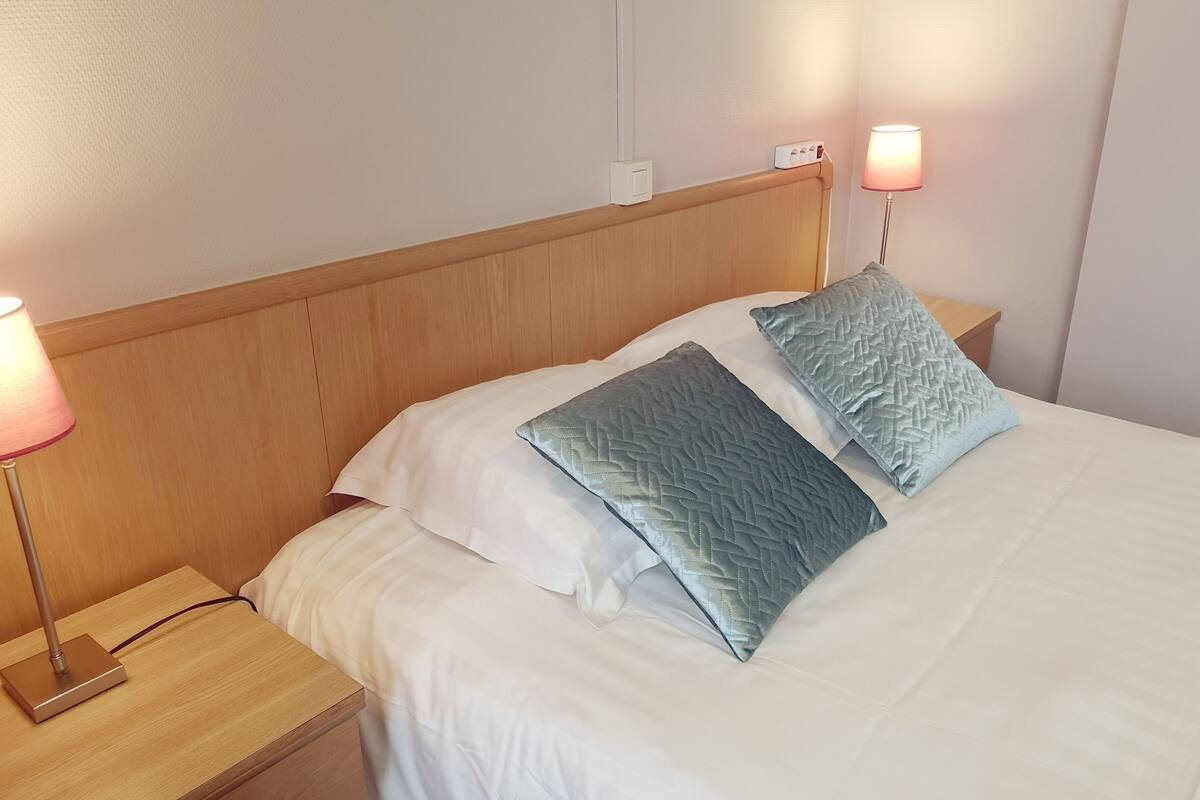 A neatly made bed with two pillows, a bedside lamp, and a wooden nightstand.