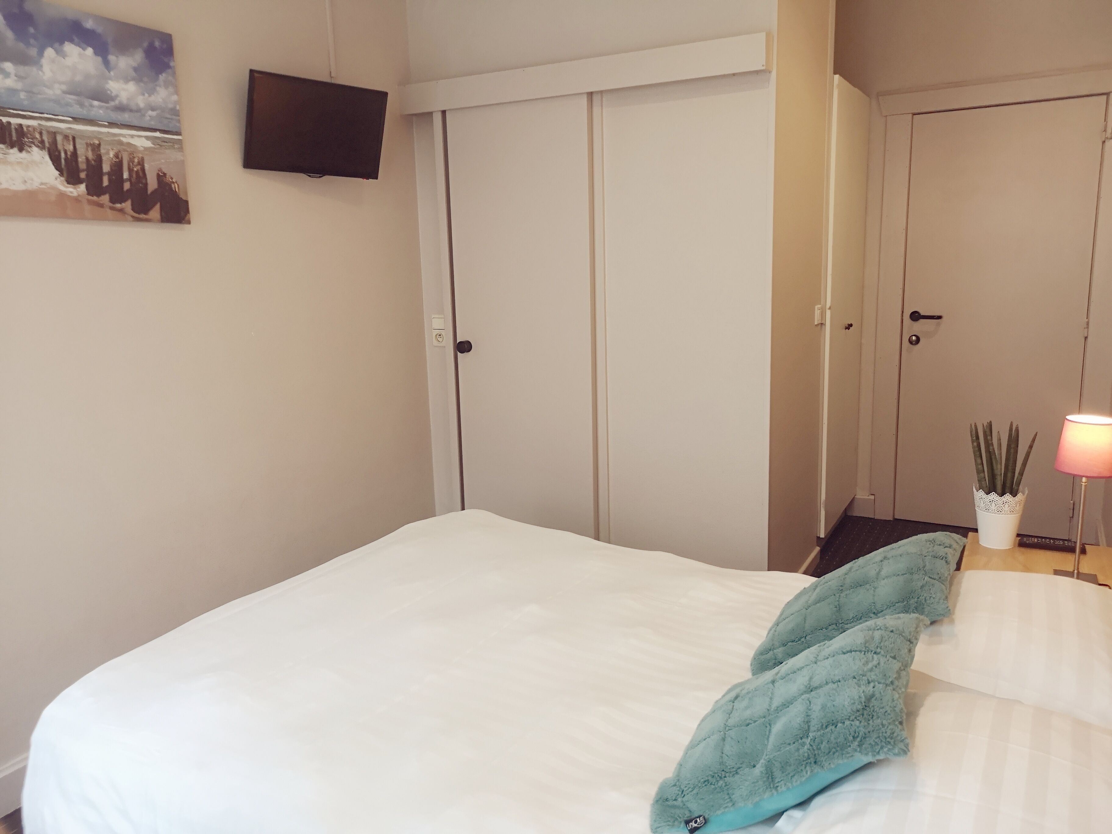 Un dormitorio con una cama, un televisor montado en la pared y una puerta con manija.