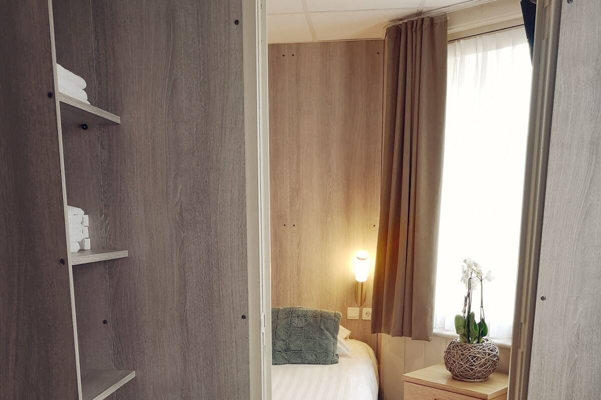 A hotel room with a bed, bedside table, lamp, and a view of the outdoors.