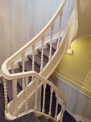 A staircase with white balusters and dark steps, leading to a landing with a striped wall.