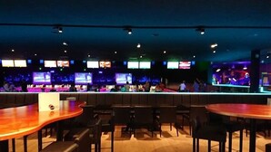 A bar area with multiple screens displaying content, wooden tables, and black chairs. - Hotel Sfinx (De Panne)
