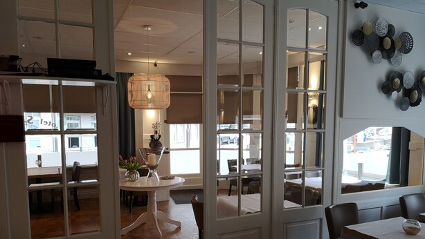 A dining area with a white table, chairs, and a hanging light fixture. - Hotel Sfinx (De Panne)