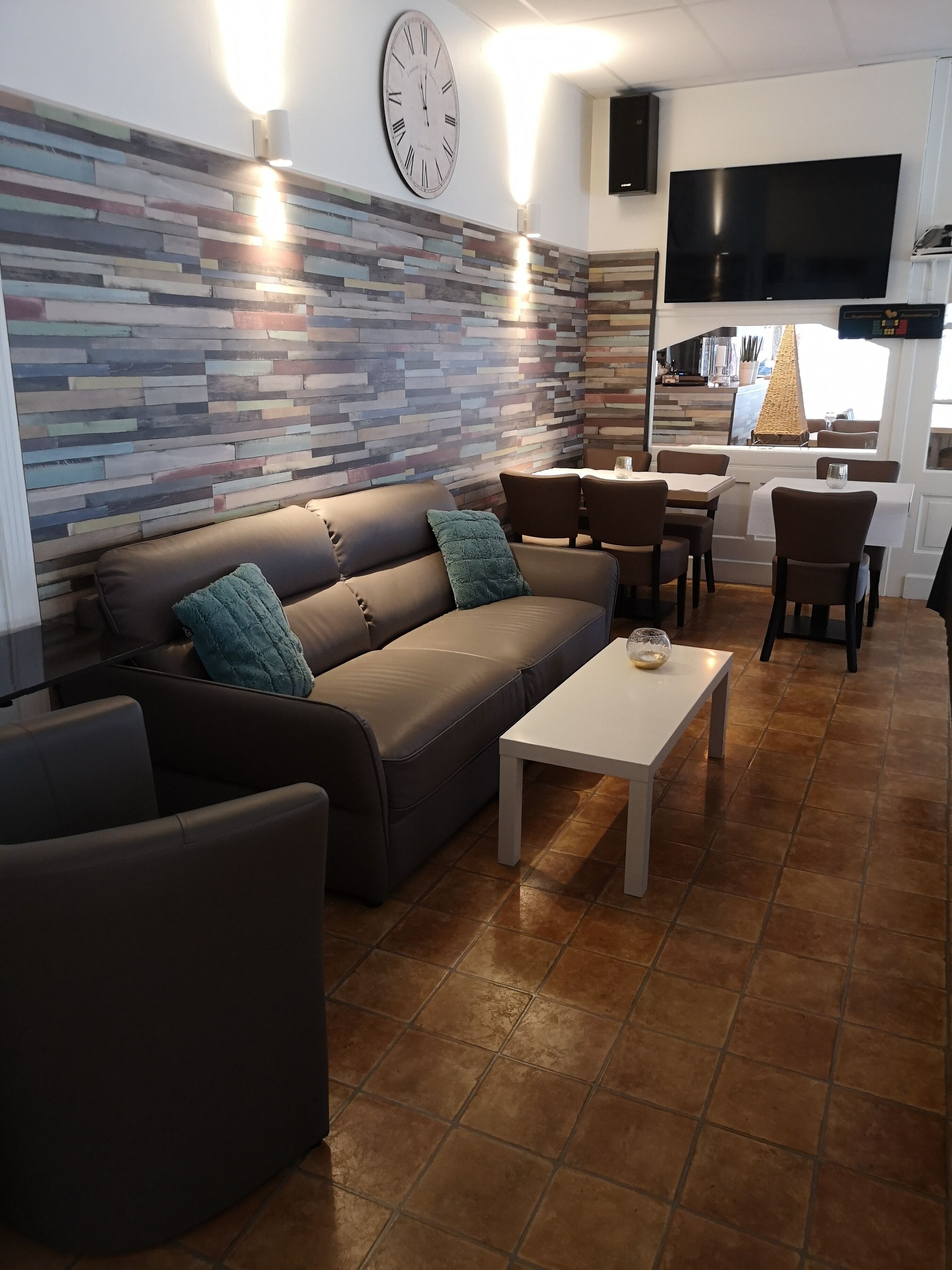 A modern living room with a brown leather sofa, teal cushions, a white coffee table, and a wall clock.
