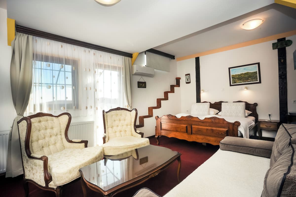 A room with a wooden bed, two armchairs, a glass coffee table, and a staircase.
