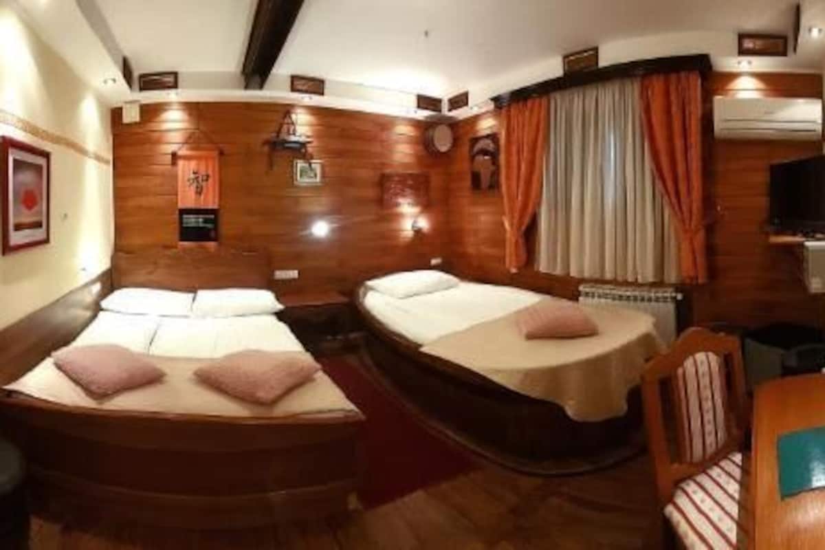 A room with two beds, a wooden floor, a mirror, and a small table.