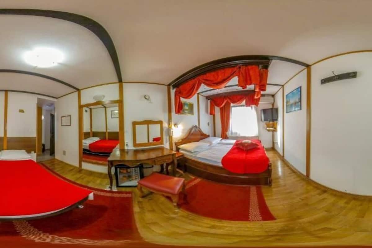 A room with a bed, a desk, and a chair. There is a window with curtains.