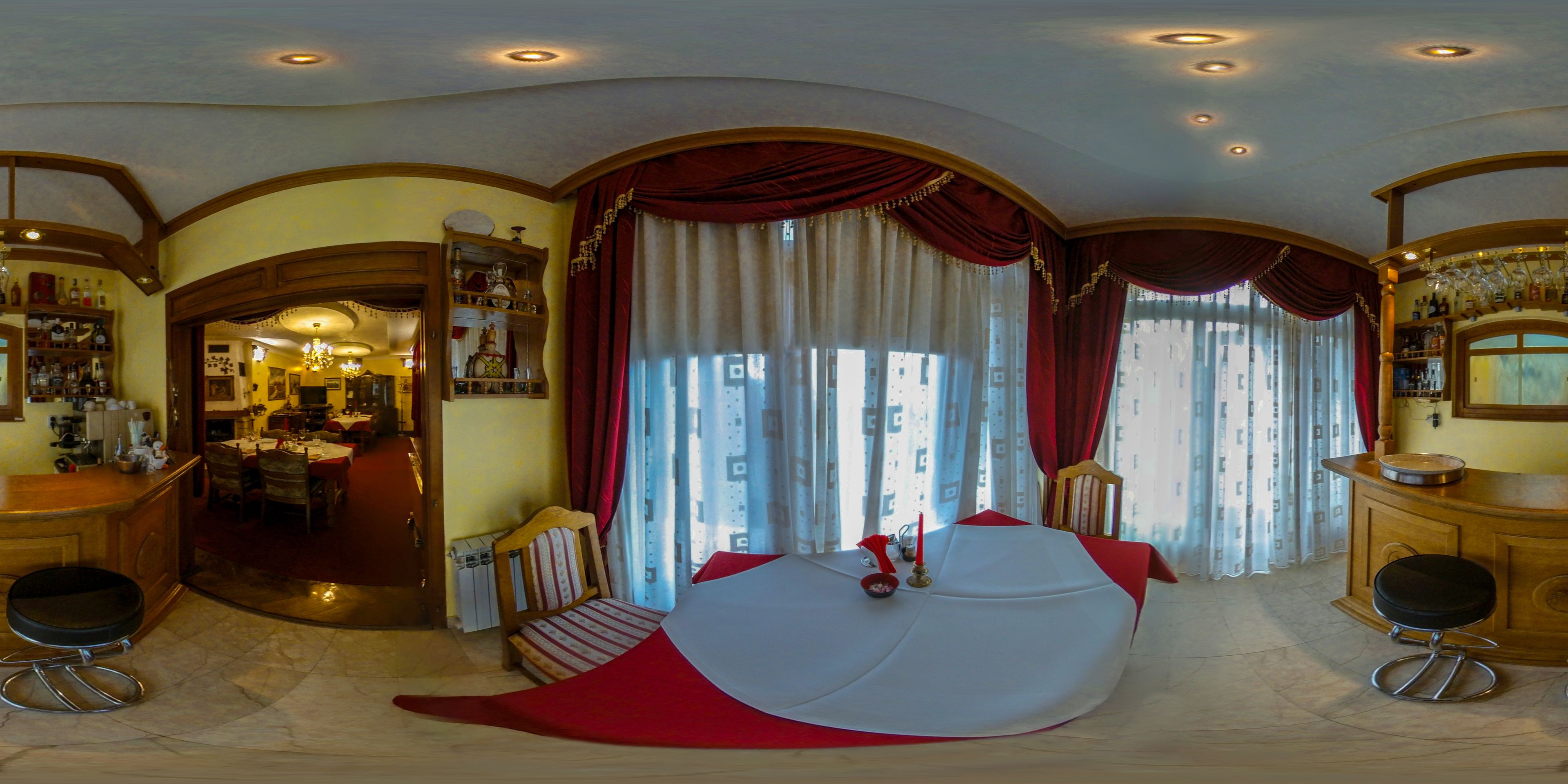 Un vaste espace de vie comprenant un grand canapé rouge et blanc, une table à manger et un coin bar agrémenté d’un lustre.