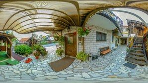 A covered outdoor area with a stone floor, a wooden bench, and a staircase leading to an upper level. - Hotel Garten (Slavonski Brod)