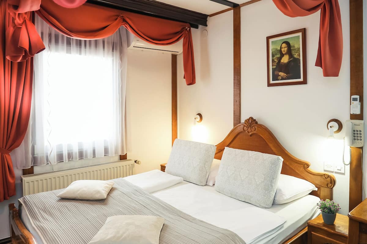 A hotel room with a large bed, a wooden headboard, a nightstand with a lamp, a telephone, and a painting on the wall.