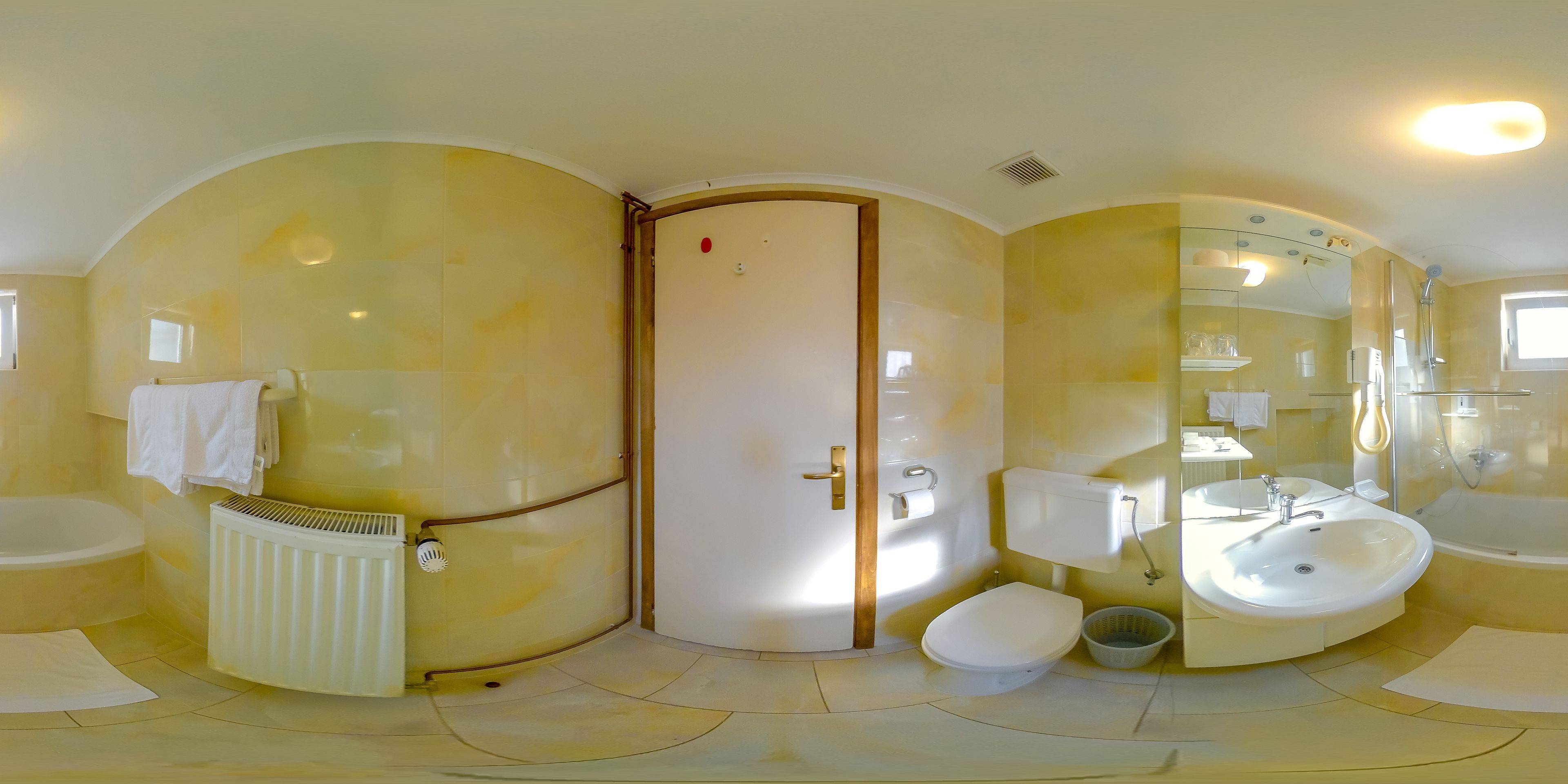 Un baño con bañera, inodoro y lavamanos, con un espejo curvo y un radiador.