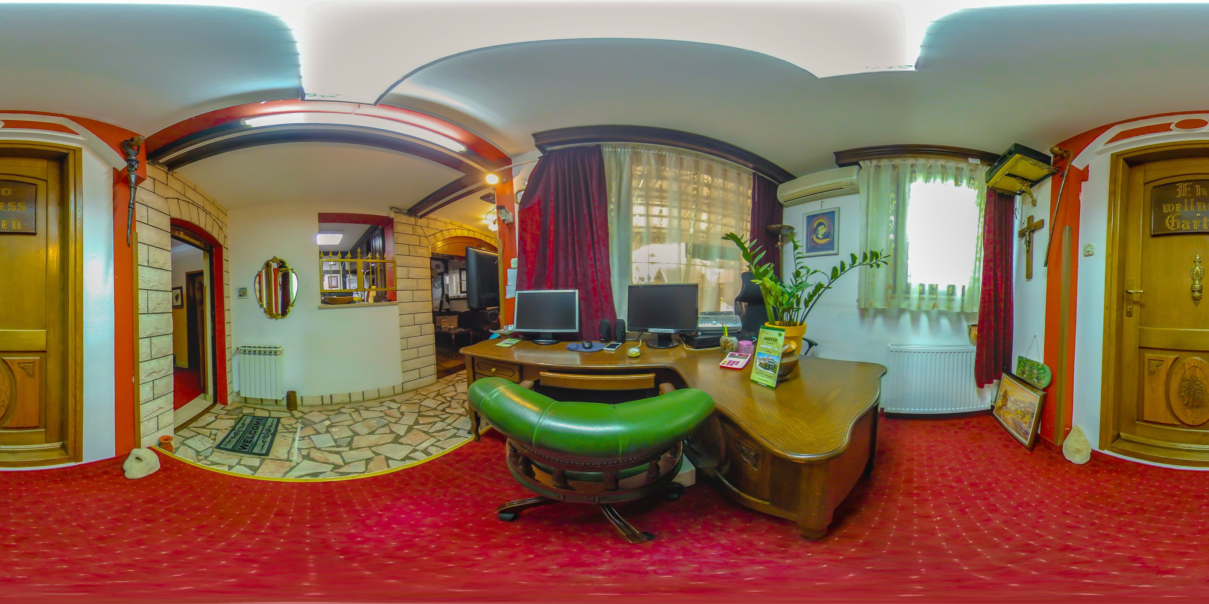 A room with a desk, two monitors, a green chair, a red carpet, and a wooden door.