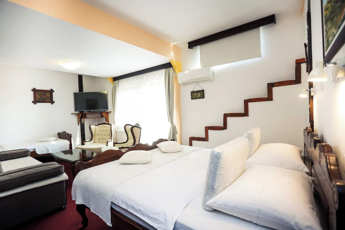 A hotel room with a large bed, a sofa, a TV, and a staircase.
