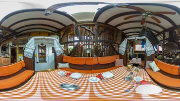 A dining area with a checkered tablecloth, orange cushioned seating, and a ceiling fan.