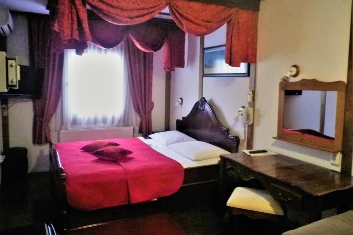 A hotel room with a bed, a desk, a chair, a mirror, and a window with curtains.
