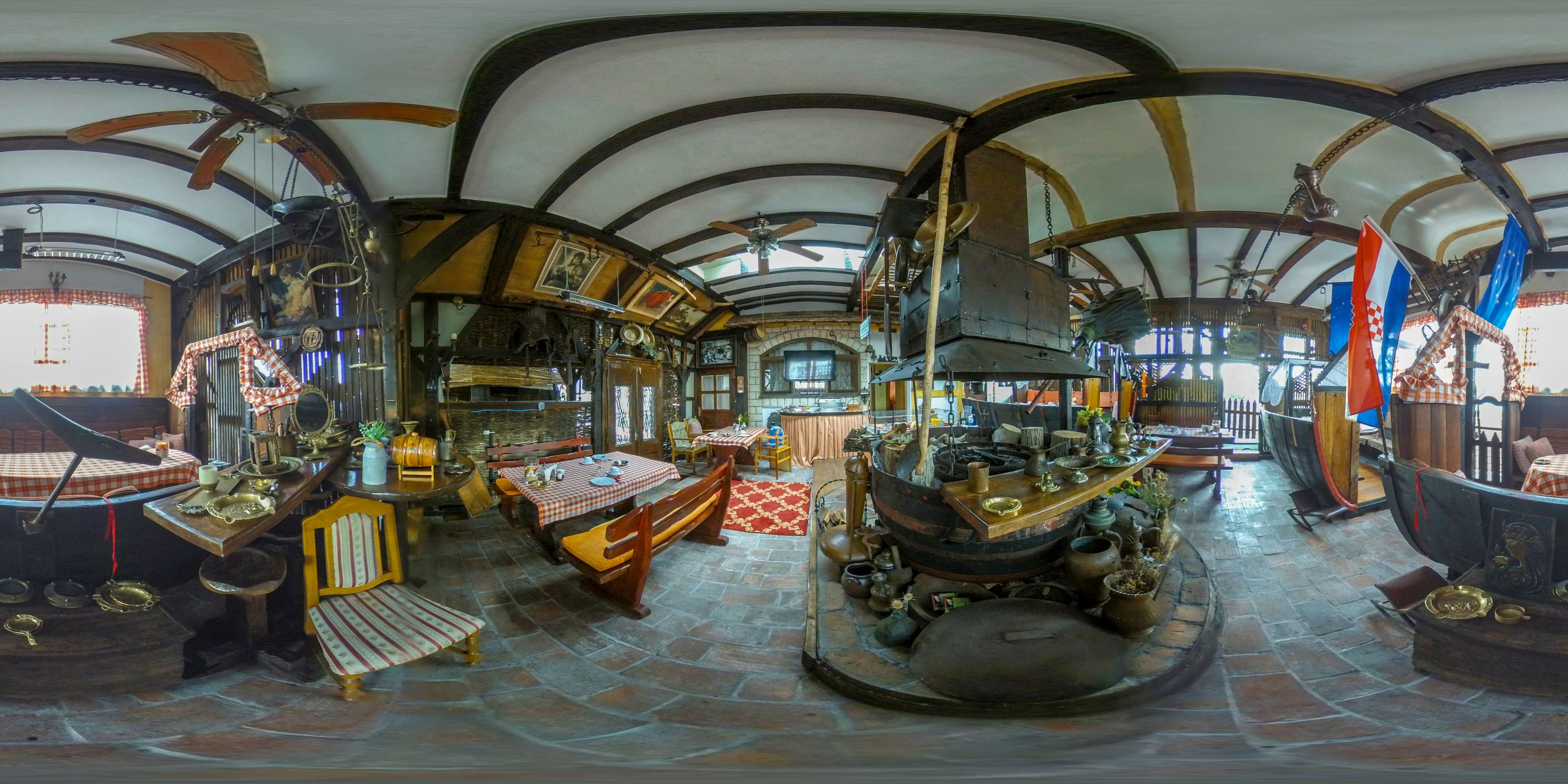 A room with a high arched ceiling, wooden beams, a central circular table surrounded by chairs, and various decorative items.