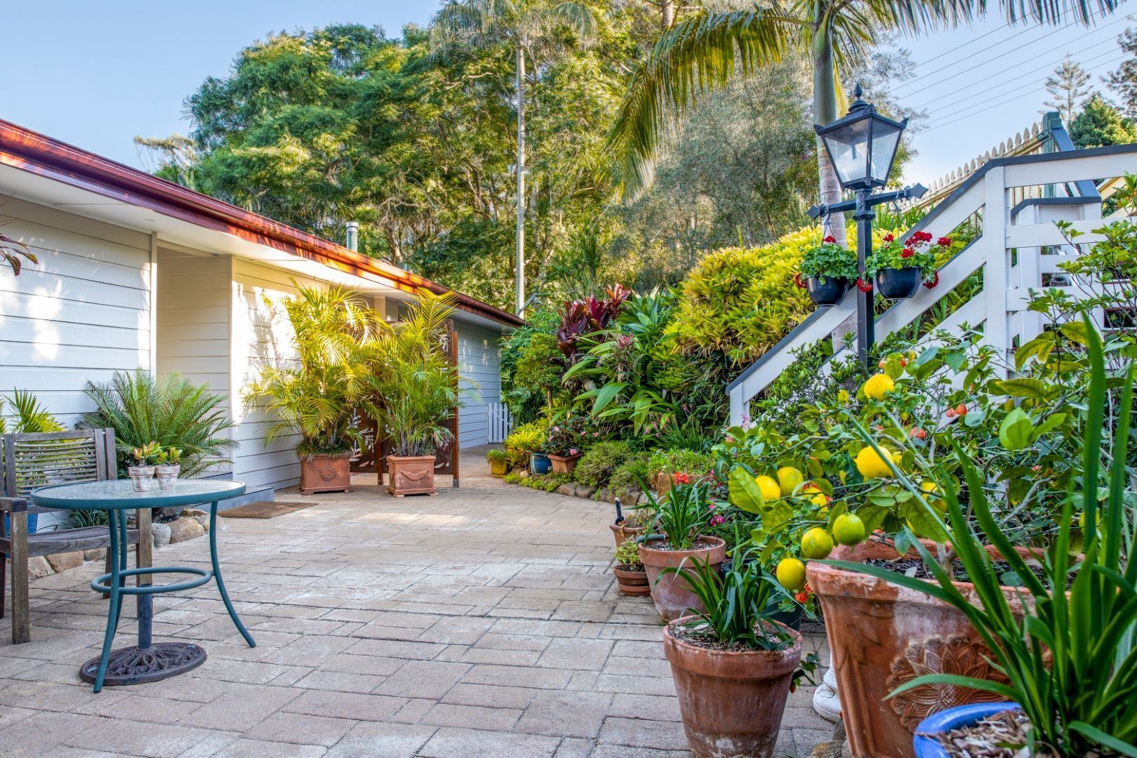A patio area with a table and chairs, surrounded by potted plants and a white fence.