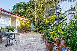 A patio area with a table and chairs, surrounded by potted plants and a white fence. - Avocado Sunset B&B (Tamborine Mountain)