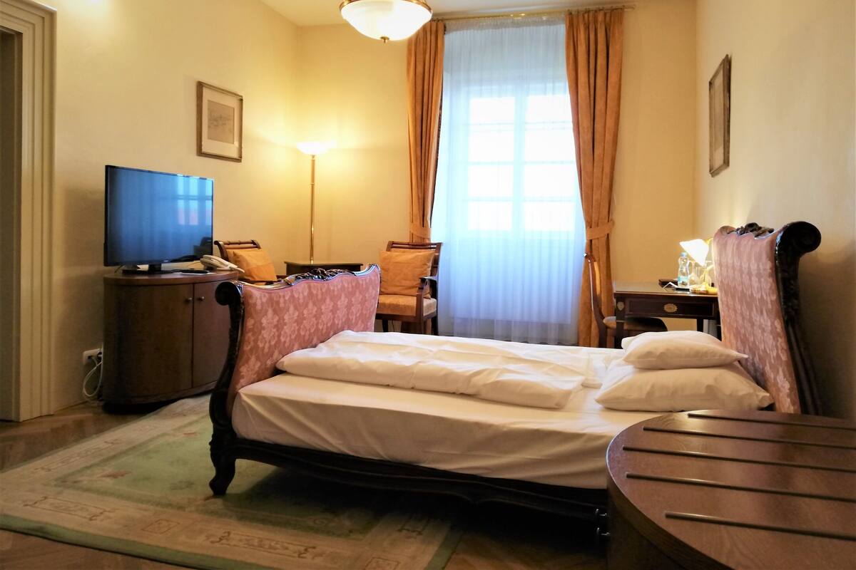 Een hotelkamer met een bed, bureau, stoel, televisie en een raam met gordijnen.