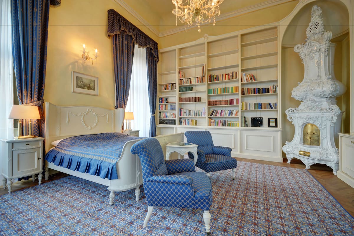 Een slaapkamer met een groot bed, twee stoelen, een boekenkast en een decoratieve vaas.