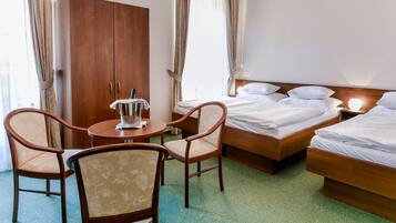Una habitación de hotel con un armario de madera, una mesa redonda con dos sillas, una cama con ropa blanca y una lámpara de noche.