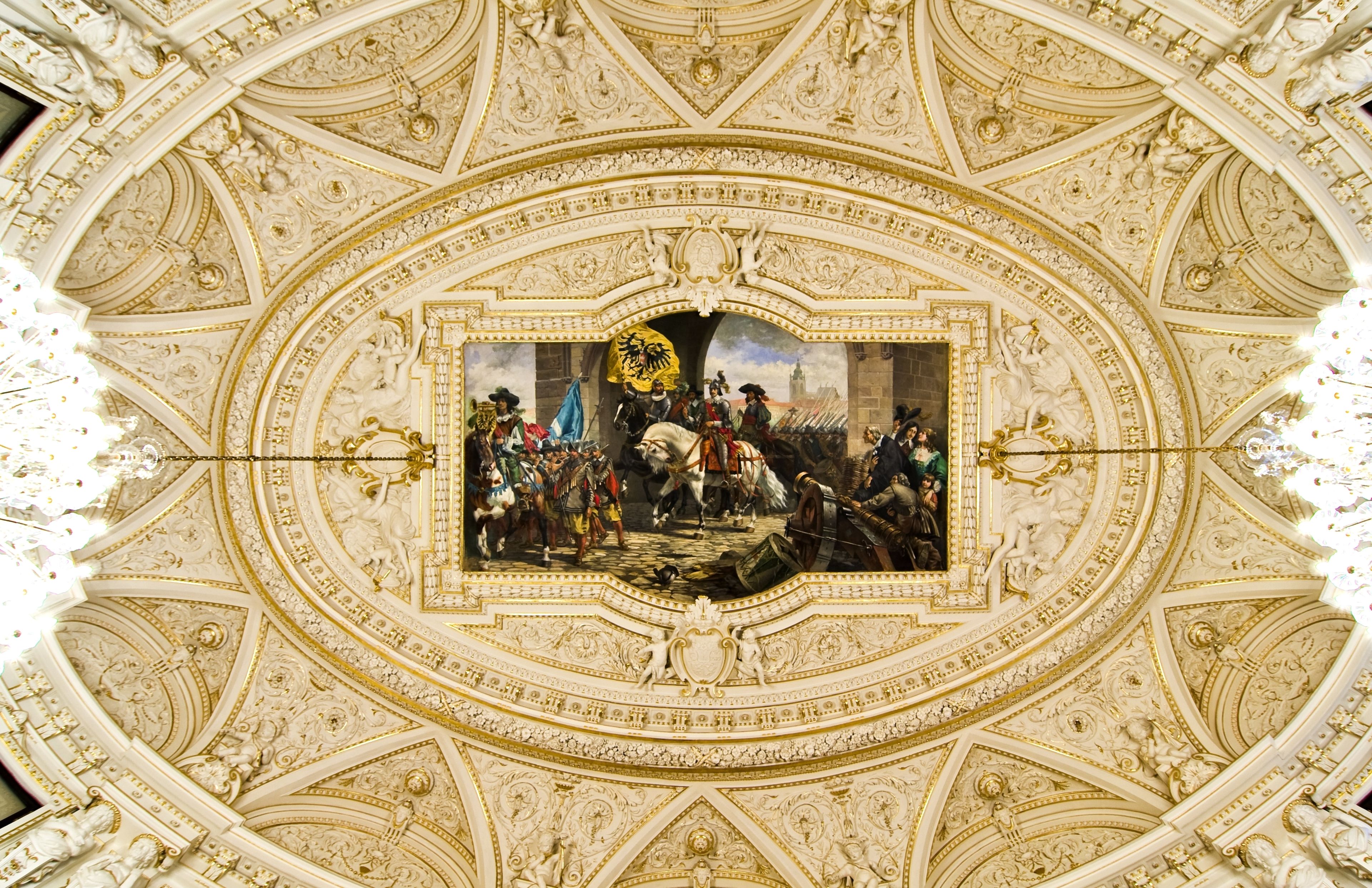 A highly ornate ceiling with intricate gold detailing and a central fresco depicting a historical scene.