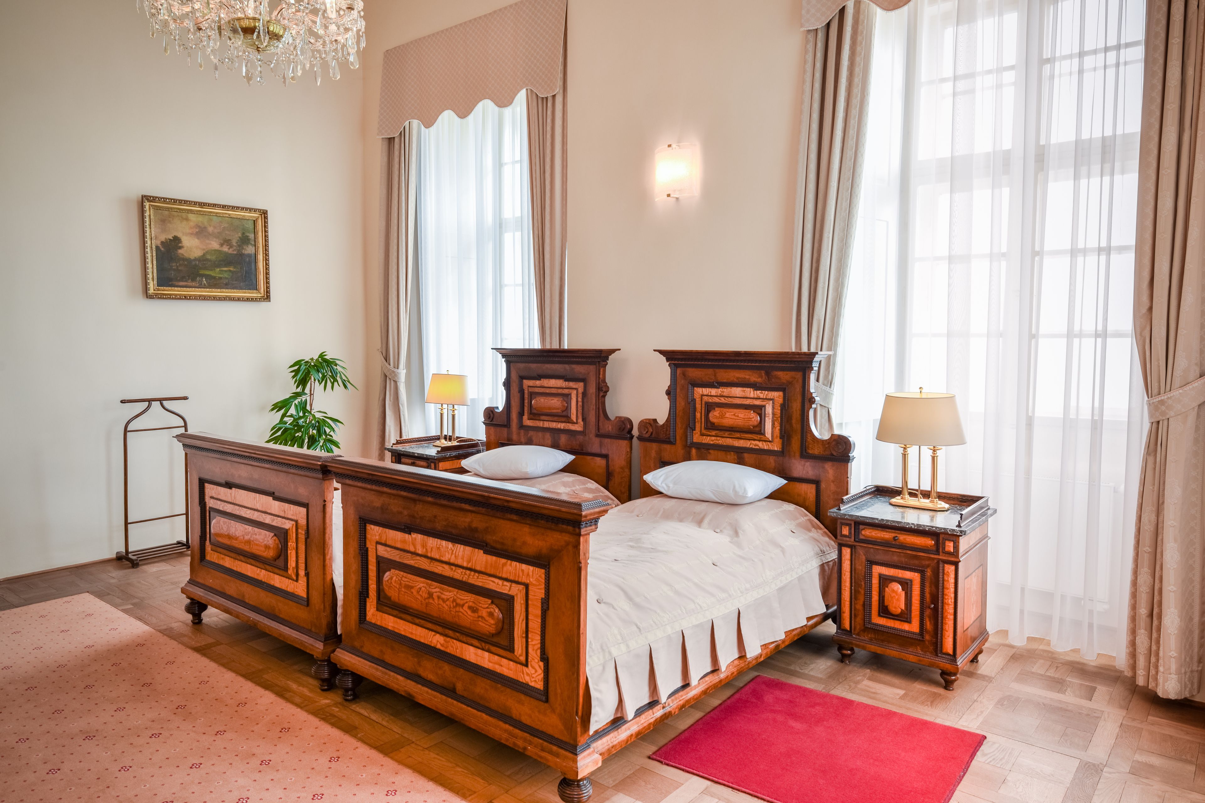 Una camera da letto tradizionale con un letto a baldacchino, due comodini, un tappeto rosso, una pianta in vaso e un quadro appeso al muro.