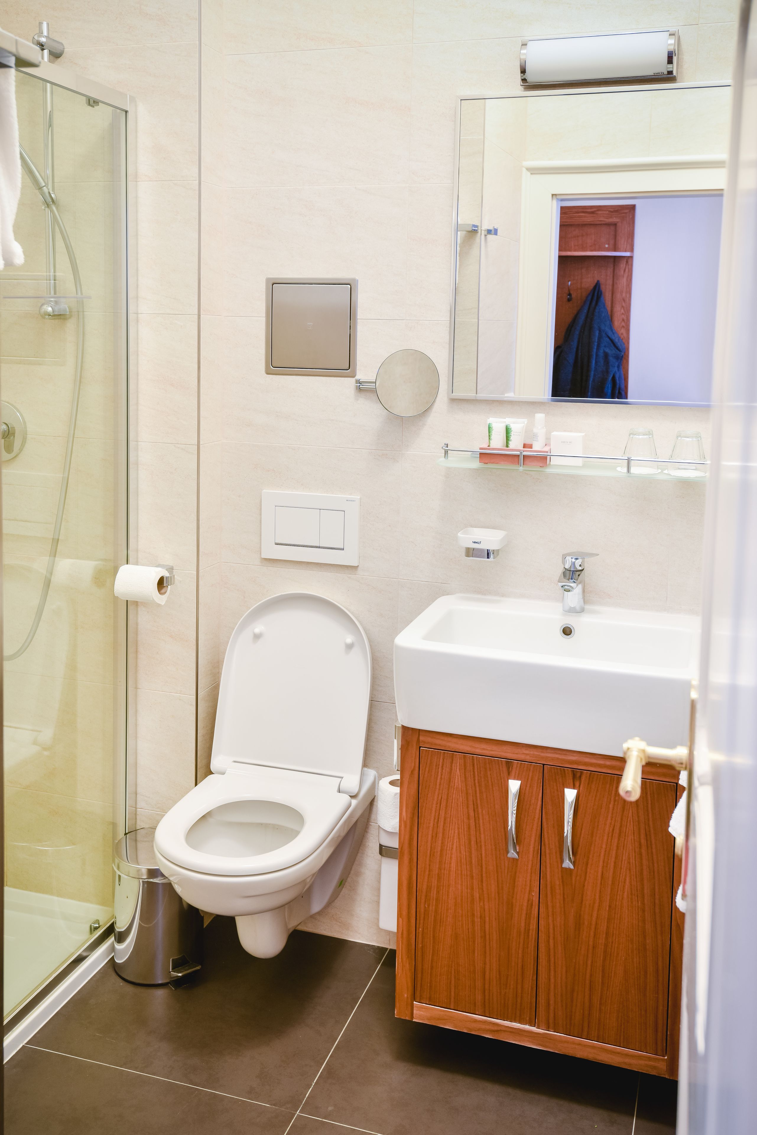 Un baño moderno con cabina de ducha de vidrio, inodoro blanco, lavabo con mueble de madera y espejo sobre el lavabo.