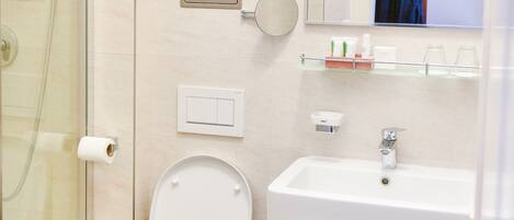 Un baño moderno con cabina de ducha de vidrio, inodoro blanco, lavabo con mueble de madera y espejo sobre el lavabo.