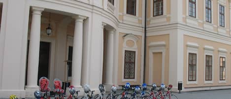 Une rangée de vélos est garée devant un bâtiment à l’architecture classique, avec des colonnes et des fenêtres décoratives.