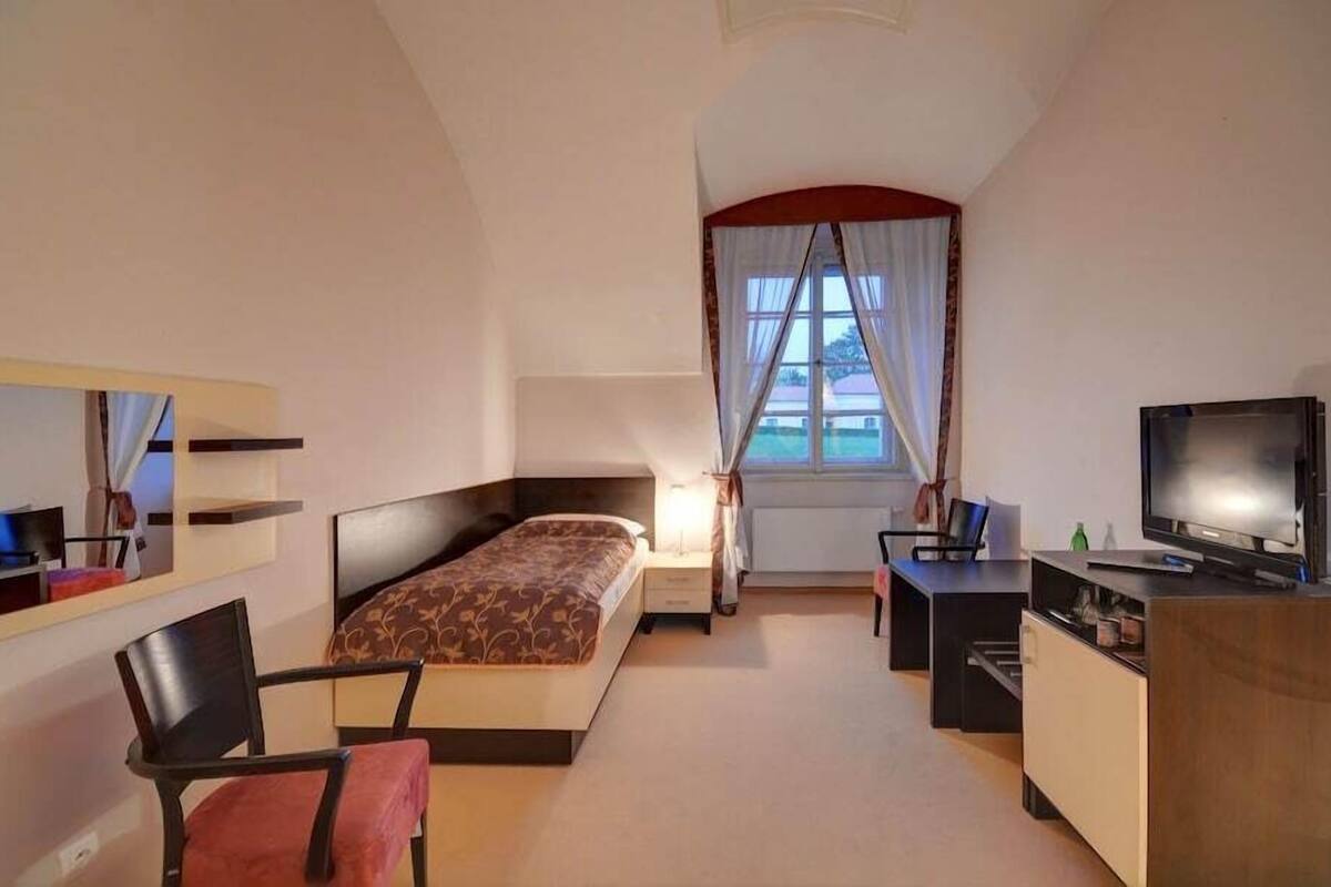 Een hotelkamer met een bed, een bureau, een stoel, een televisie en een raam met gordijnen.