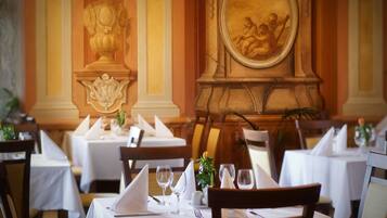 A restaurant with tables set for dining, featuring a classical architectural design with ornate decorations and a mural on the wall.