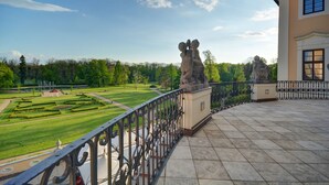 Un balcon donnant sur un jardin magnifiquement entretenu et orné d’une statue.