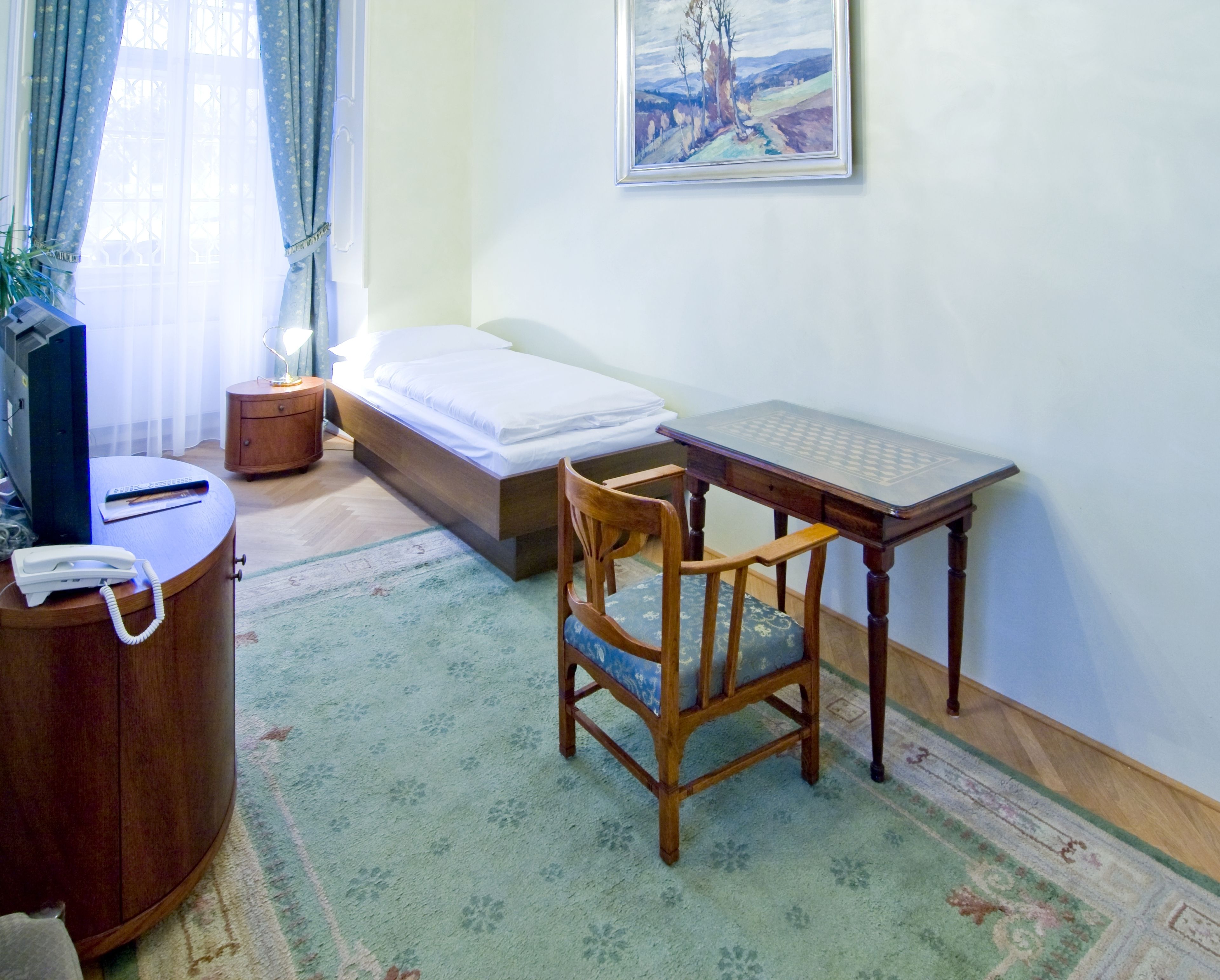 Ein Zimmer mit einem Bett, einem Schreibtisch, einem Stuhl, einem Telefon, einer kleinen Kommode und einem Bild an der Wand.
