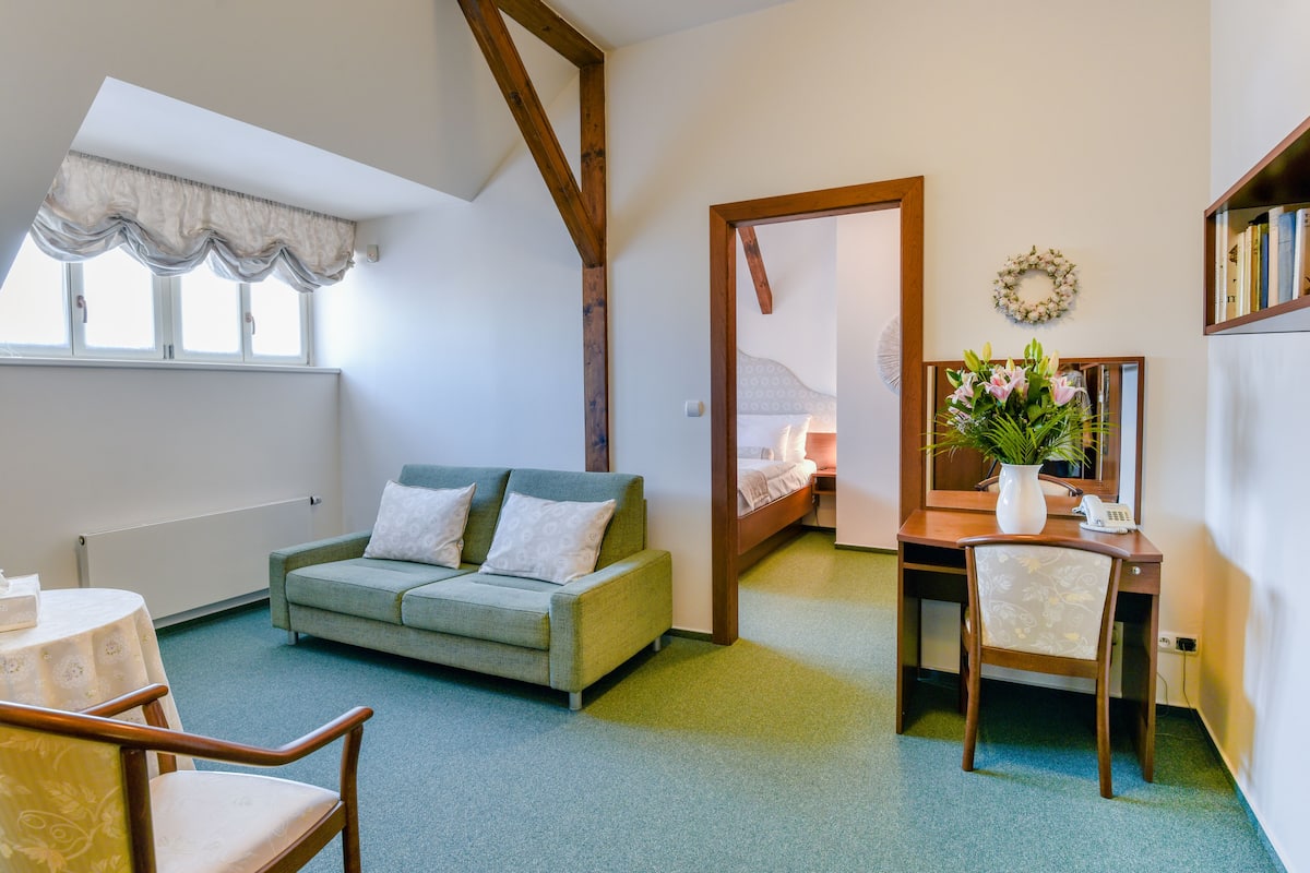 Een gezellige kamer met een groene bank, een houten bureau, een stoel, een kleine tafel en een bed op de achtergrond.