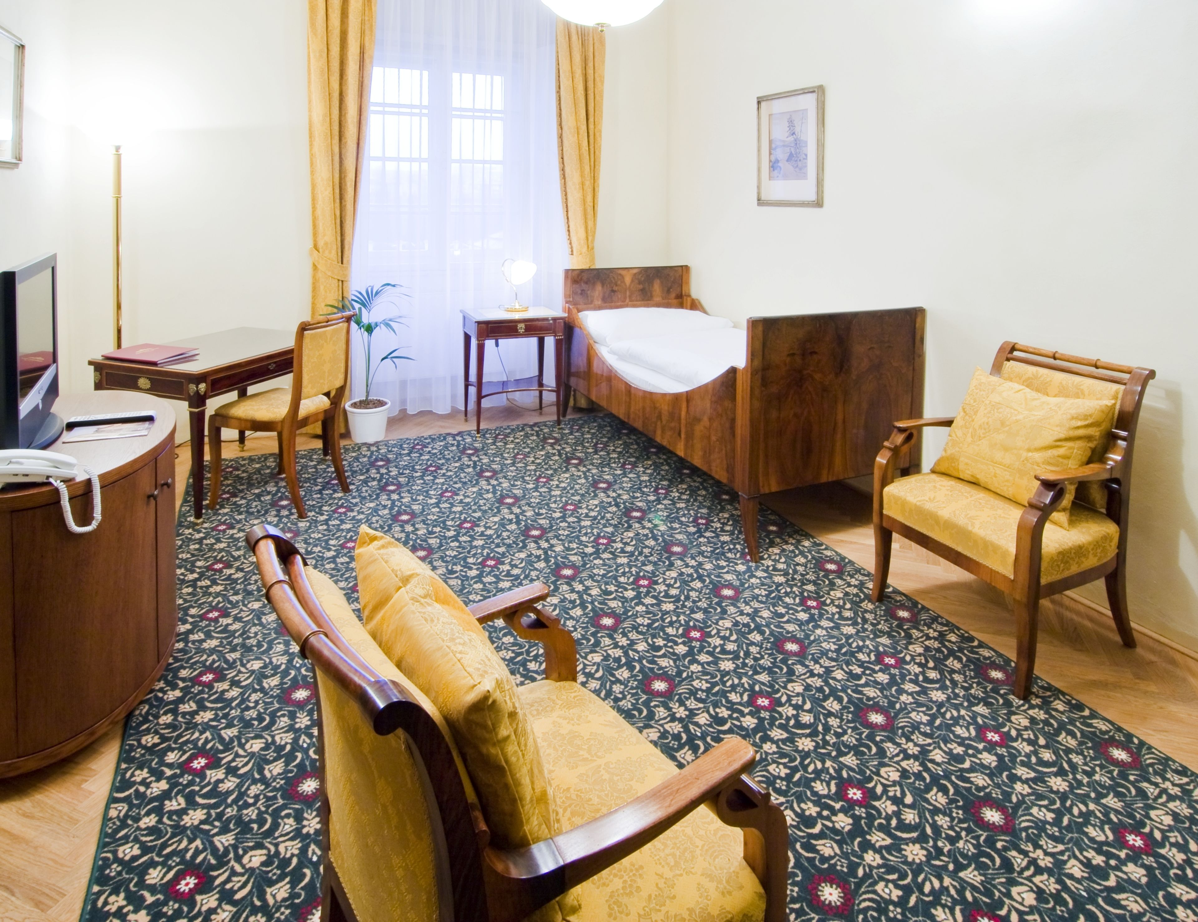 A hotel room with a bed, a desk, a chair, a television, and a potted plant.