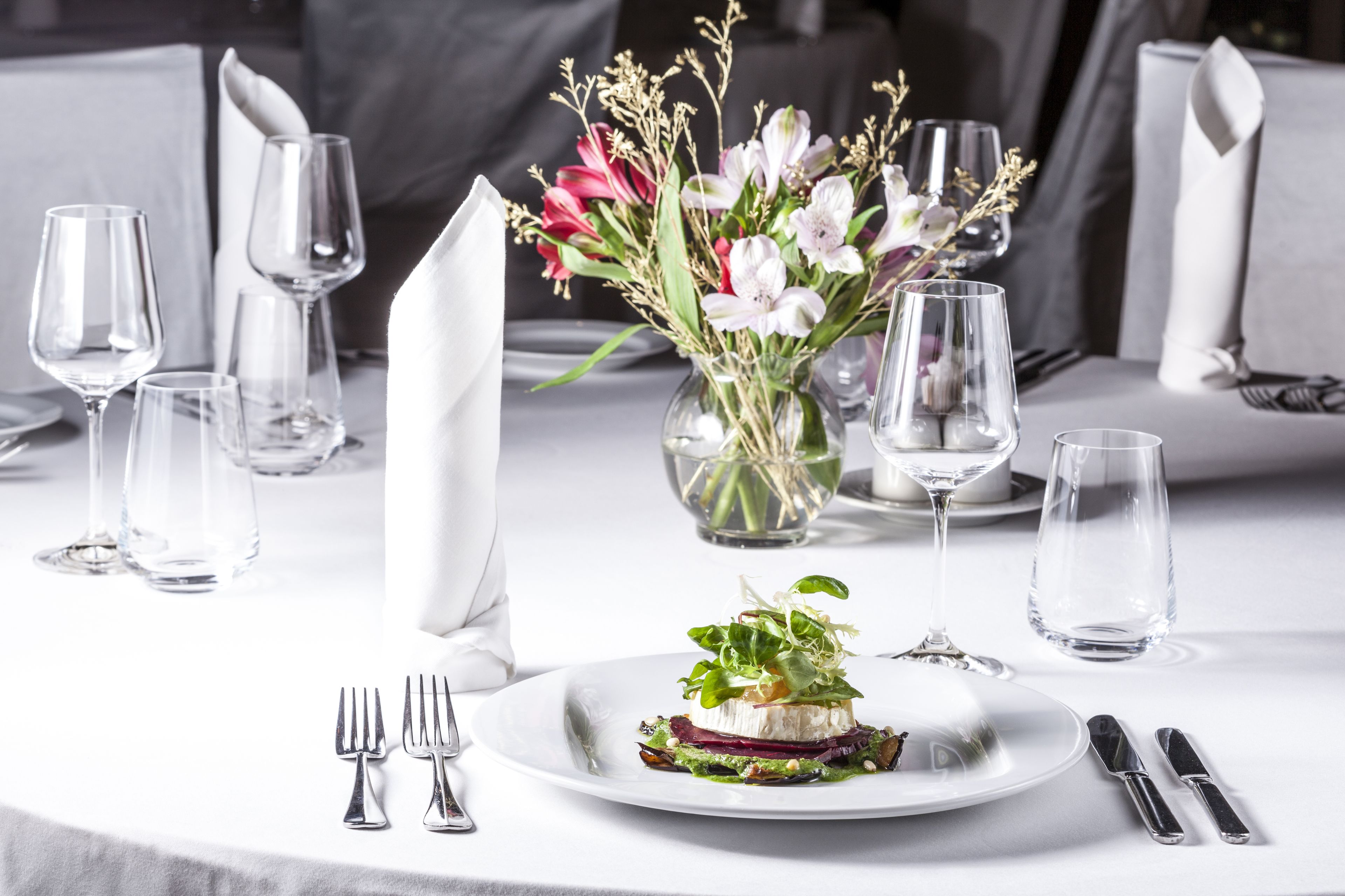 A dining table set with a white tablecloth, a vase of flowers, and a plate of food.
