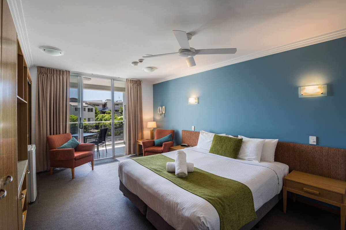 A hotel room with a large bed, a ceiling fan, a desk, and a chair.