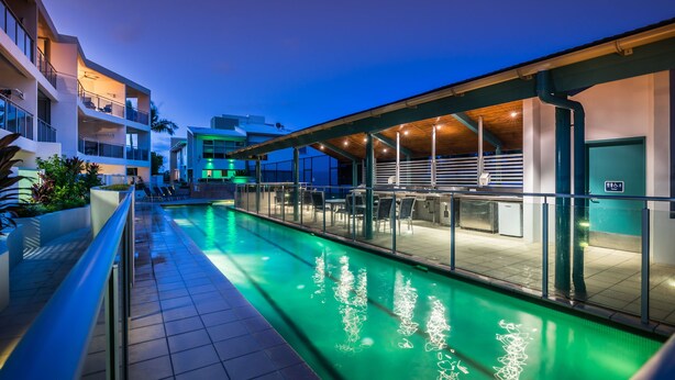 Un hôtel moderne doté d’une piscine, d’un espace extérieur aménagé et d’une zone couverte avec des tables et des chaises.