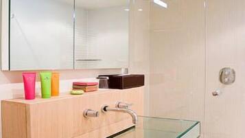 A modern bathroom with a glass shower enclosure, a glass sink, and a mirrored vanity with toiletries.