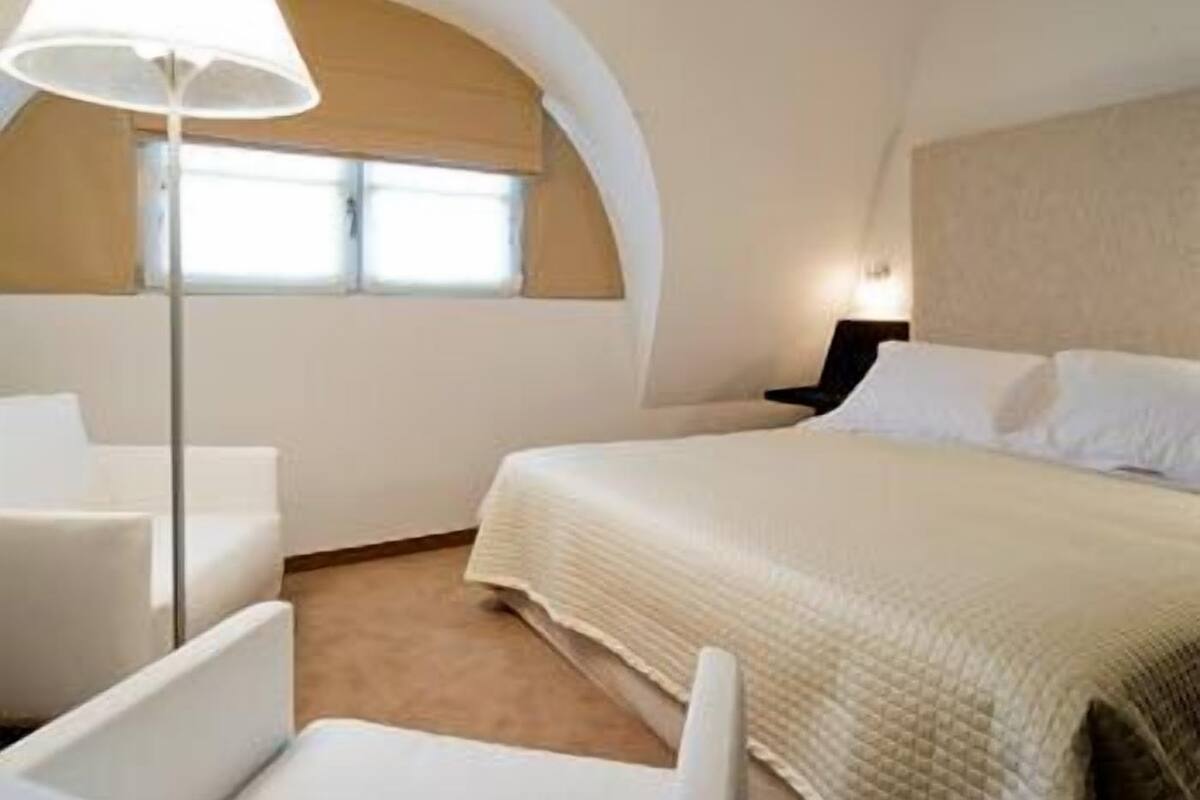 A hotel room with a bed, a desk, a chair, a lamp, and a window with curtains.