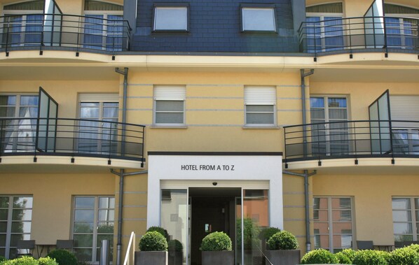 A multi-story hotel with balconies, a sign reading "HOTEL FROM A TO Z", and a glass entrance. - Hotel Alzinn (Hesperange)