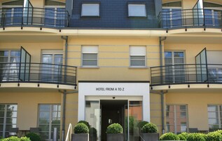 Un hotel de varios pisos con balcones, un cartel que dice "HOTEL FROM A TO Z" y una entrada de cristal.